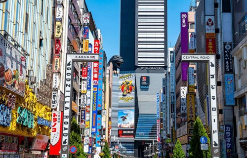 Bustling street scene in Japan with modern buildings and colorful billboards, figure of Godzilla