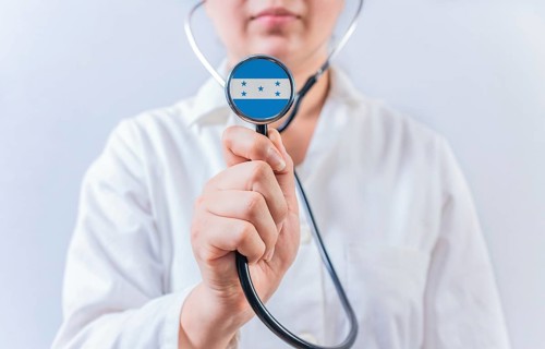 Female doctor holding stethoscope with Honduras flag. National health system of Honduras