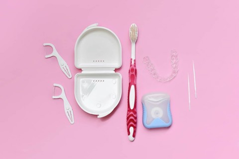 Top view of dental clear aligners, toothbrush, toothpicks and floss on pink background with copy