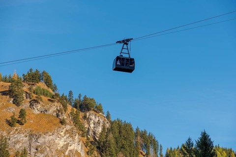 A Tegelbergbahn cabin floats over a mountainous landscape under a clear blue sky, near Schwangau,