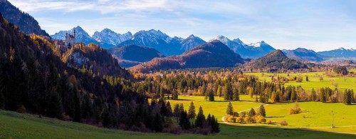 Panoramic picture, vast landscape with green fields, the distant Neuschwanstein Castle and majestic