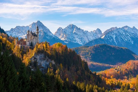 The majestic Neuschwanstein Castle on a mountain with autumn-colored forest in the foreground,