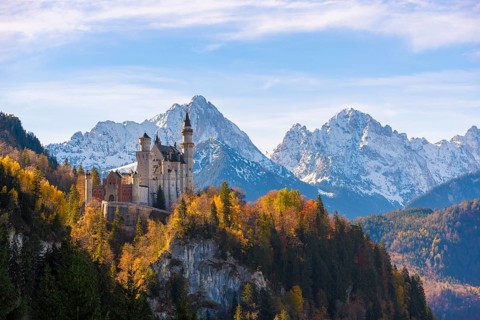 Neuschwanstein Castle stands majestically on a hill with autumn trees, surrounded by snow-capped