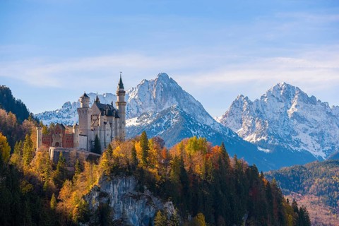 Neuschwanstein towers over an autumnal valley and magnificent snow-covered mountain formations,