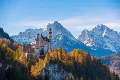 Neuschwanstein Castle surrounded by autumnal forest and high mountains, Schwangau near Füssen,