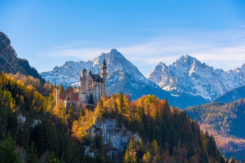 Neuschwanstein Castle rises majestically against snow-covered Alps in an autumnal landscape,