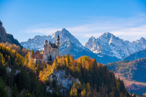 Neuschwanstein Castle towers over autumn trees against a backdrop of the Alps, Schwangau near
