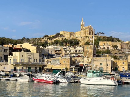 View of front sports boats sailboat in Mgarr harbour behind houses, on hills in the background