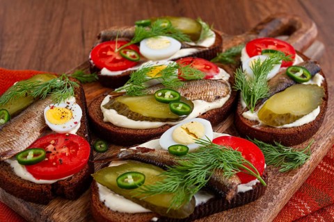 Sandwiches on rye bread with sprats, quail eggs, fresh tomatoes and pickled cucumber, on a wooden