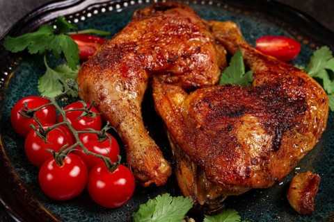 Grilled fried chicken legs, served with fresh cherry tomatoes and herbs, on a plate, homemade, no