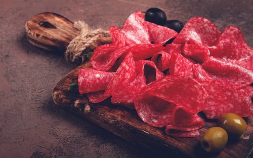 Sliced salami sausage, on a wooden chopping board, decorated with olives and herbs, close-up, no