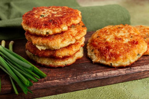 Crispy potato pancakes Latkes, stacked on a wooden board next to fresh green onions, natural light,