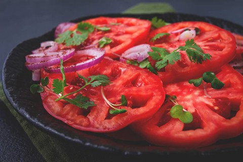 Freshly sliced tomatoes and red onions, garnished with herbs, on a black plate, summer salad, no