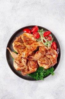 Baked quail, served on a plate with crispy lettuce leaves, fresh tomatoes and herbs, on a dark
