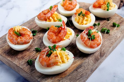 Boiled eggs stuffed with yolk and seasoned with mayonnaise, stuffed eggs with shrimp, on a wooden