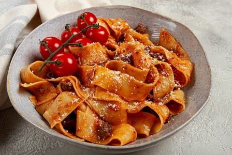 Pappardelle pasta with bolognese sauce, topped with parmesan cheese and cherry branch, homemade, no
