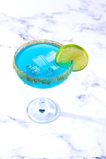 Bright blue cocktail with a slice of lime on a marble surface