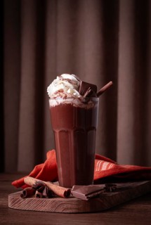 Hot chocolate drink, topped with whipped cream, chocolate shavings, and a cinnamon stick
