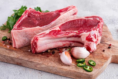 Fresh pieces of beef on the bone, on a wooden cutting board, with herbs and spices, ready for