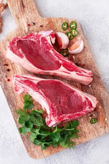 Fresh pieces of beef on the bone, on a wooden cutting board, with herbs and spices, ready for