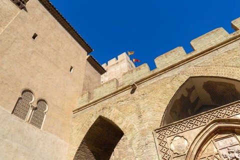 Looking up at historic tower and ramparts in courtyard of historic castle, Aljafería Palace,