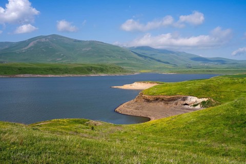 A calm lake surrounded by green hills and mountains under a blue sky with clouds, Spandaryan