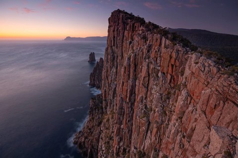 Long exposure at sunrise shows the glowing dawn over the huge rocks of Cape Hauy. Waves hit the