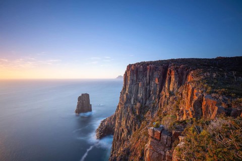 Long exposure at sunrise shows glowing dawn over the dramatic cliffs of Cape Hauy. View towards