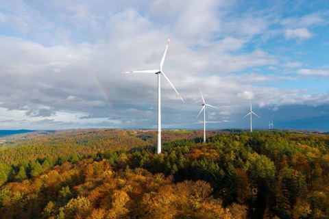Wind turbines rise above an autumnal forest with a rainbow in the background, near Schorndorf,
