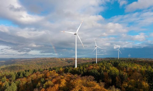 Wind turbines stand over an autumnal forest with a rainbow in the sky, near Schorndorf, Remstal,