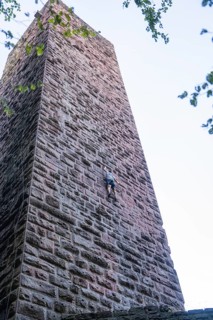 A climber climbs the stone wall of a tower, accentuated by clear air and natural surroundings,