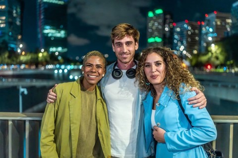 Diverse group of three friends standing arm in arm, smiling at the camera during a casual night out
