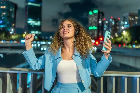 Young woman with curly hair wearing headphones and holding a smartphone, actively dancing to music