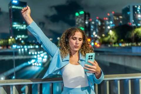 Young woman with curly hair wearing headphones and an elegant blue outfit, expressing joy and