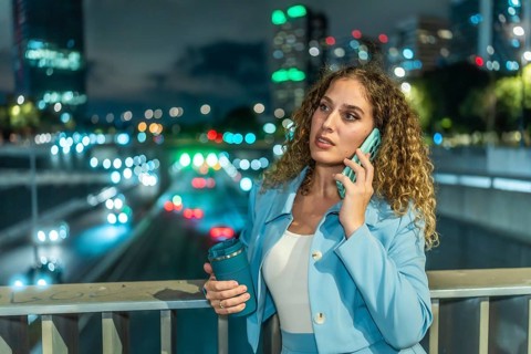 Professional businesswoman standing on a city bridge at night, having an important phone call with