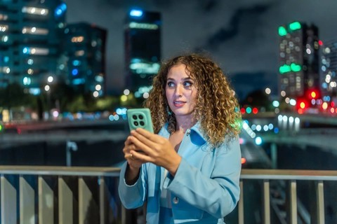 Young woman with curly hair looking surprised while holding a mobile phone, discovering new content