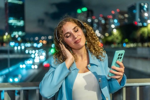 Young woman with curly hair finding joy and relaxation listening to music using headphones and a