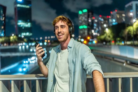 Smiling young man wearing headphones and holding a smartphone, happily listening to music while