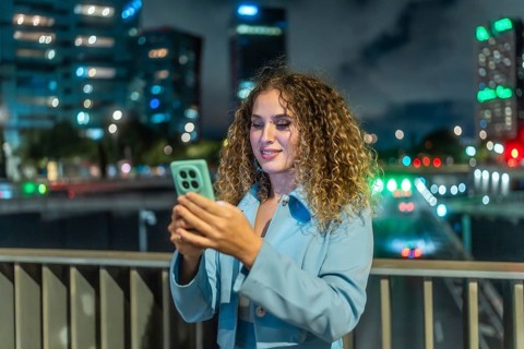 Young woman smiling, scrolling on her smartphone, enjoying connectivity and social media on a city