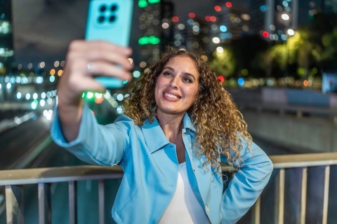 Young woman with curly hair smiling happily while capturing a selfie on her mobile phone, standing