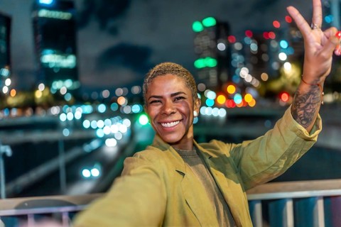 Happy young black woman taking a selfie and showing a peace sign, smiling brightly at camera,