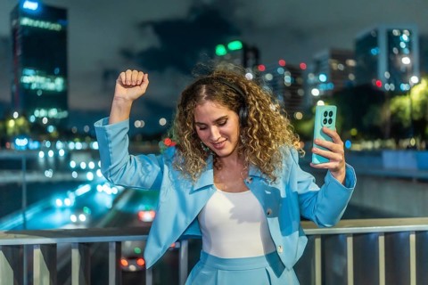 Young woman with curly hair enjoying music through headphones, holding a smartphone, and dancing