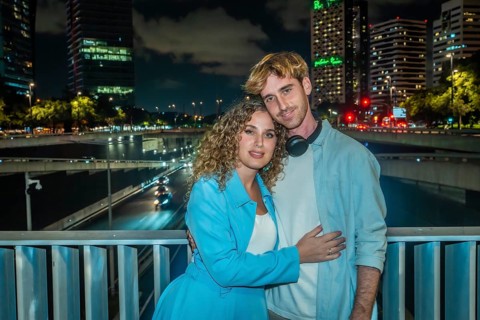 Young couple embracing on an urban bridge at night, city skyline and streaking highway lights