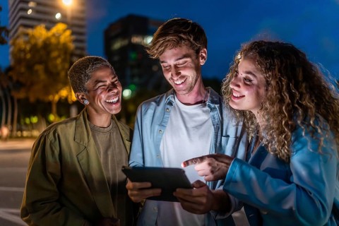 Cheerful diverse friends laughing and sharing content on a tablet while standing together on a city