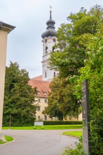 Baroque church tower behind trees and building complex in a green landscape, ZFP Zwiefalten,