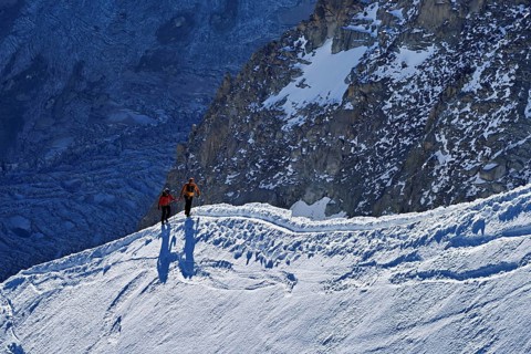 Two ascended mountaineers run across a snow-covered mountain ridge, Aiguille du Midi,