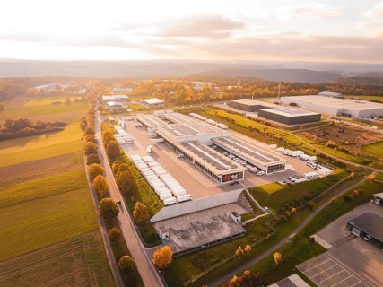 Industrial park with numerous buildings surrounded by green fields and warm skies, Nagold, Black