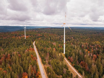 Wind turbines in colorful autumn forest with road under cloudy sky, Simmersfeld wind farm, Germany
