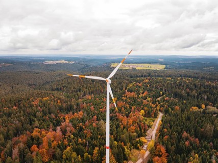 Large wind turbine over colorful autumn forest with nearby fields, Simmersfeld wind farm, Germany