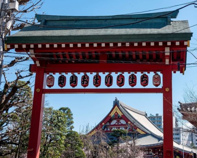 Red gate with lanterns, red and gold roof gable of a temple building, Buddhist temple complex,